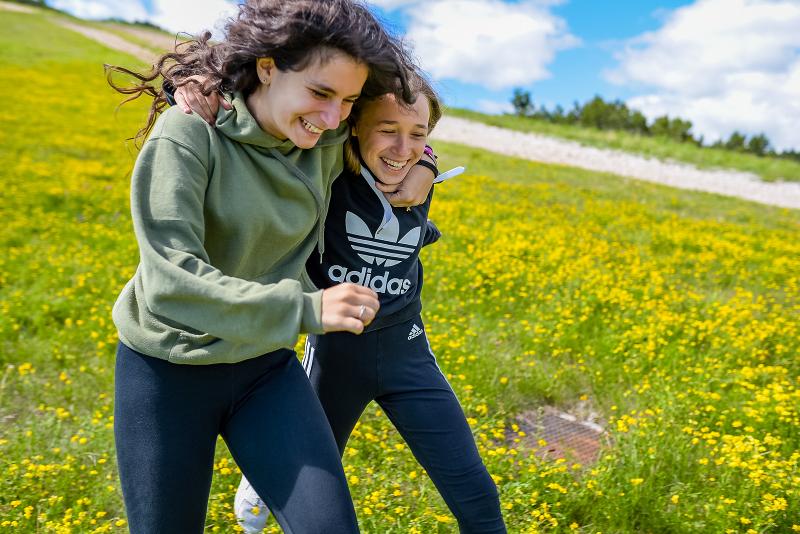 Al campo estivo teatro due ragazze si abbracciano e camminano in mezzo a un prato pieno di fiori gialli