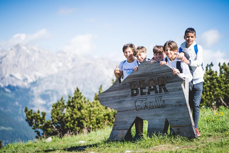 Al campo estivo in montagna per ragazzi, cinque bambini si trovano dietro a un'insegna di legno in montagna