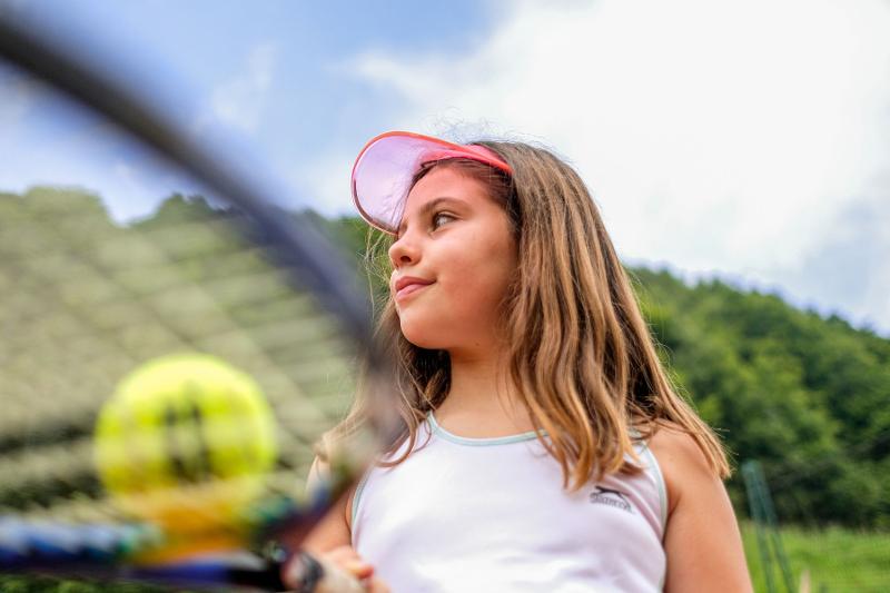 Una bambina tiene in equilibrio la pallina con la racchetta al campo estivo tennis e multisport