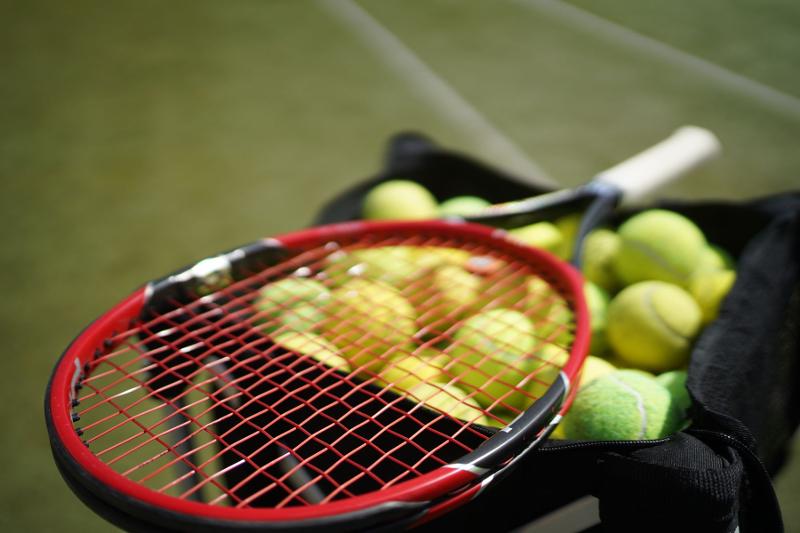 Una racchetta è appoggiata sopra la cesta delle palline al campo estivo tennis e multisport