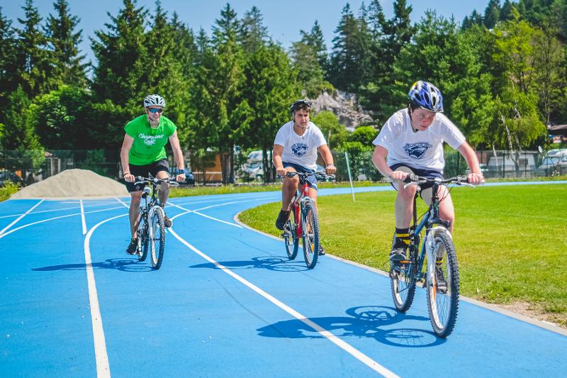 Tre ragazzi percorrono un percorso blu in bicicletta in mezzo al verde al campo estivo rugby