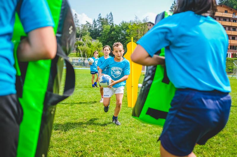 I giovani partecipanti del campo estivo rugby si allenano sugli sfodnamenti aiutati da cuscini protettivi