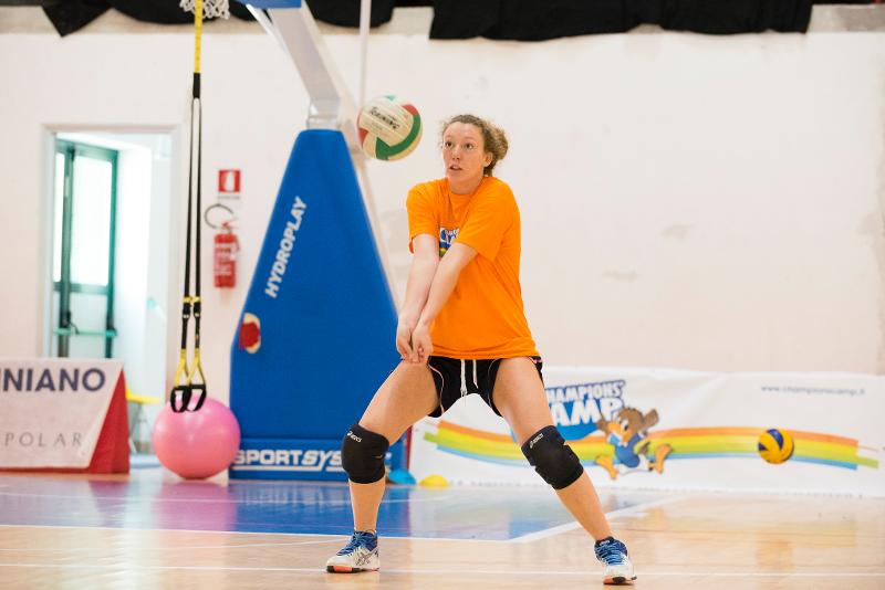 Al campo estivo pallavolo una ragazza vestita di arancione esegue un bagher sul campo da gioco