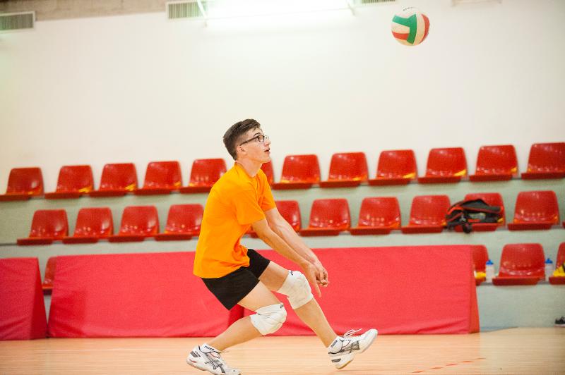 Un ragazzo vestito di arancione e con le ginocchiere bianche e gli occhiali esegue un bagher al campo estivo pallavolo