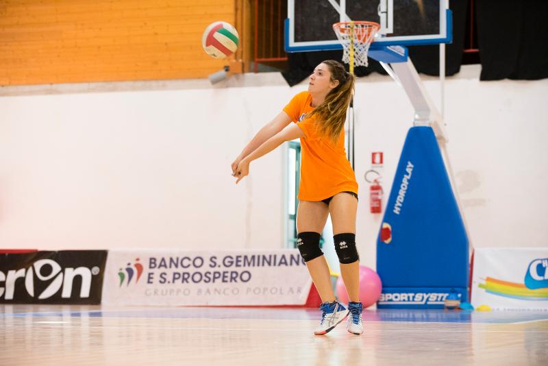 Al campo estivo pallavolo una ragazza vestita in arancione esegue un bagher colpenso la palla 