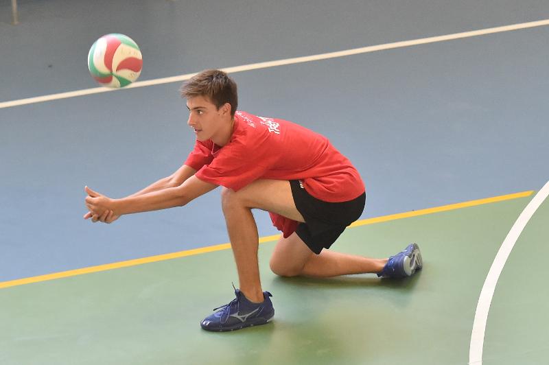Al campo estivo pallavolo un ragazzo vestito di rosso si china sulle ginocchia per eseguire un bagher