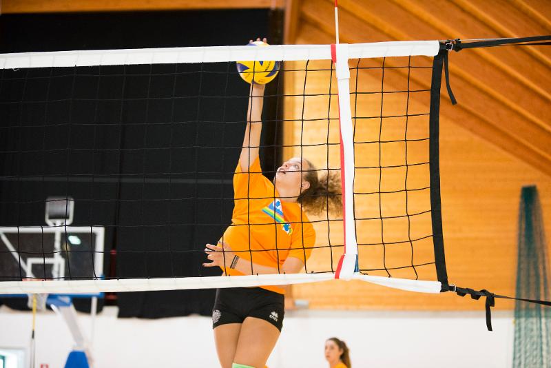 Al campo estivo pallavolo una ragazza in arancione salta e colpisce la palla in schiacciata