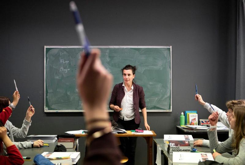 I ragazzi alzano la mano impugnando una penna mentre l'insegnante sta in piedi vicino alla cattedra al soggiorno linguistico Belgio