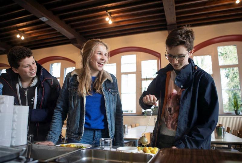 Al soggiorno linguistico in olandese, tre ragazzi nella mensa si stanno servendo il cibo sorridendo