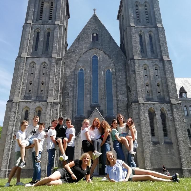 Gruppo di ragazzi posa di fronte ad una cattedrale sul prato in una giornata di sole ai campi estivi Belgio