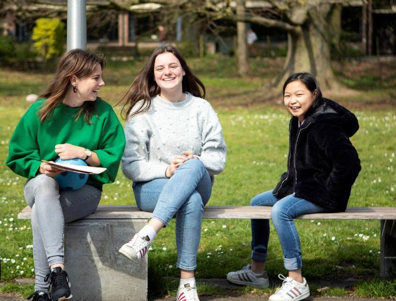 Al soggiorno linguistico Belgio tre ragazze siedono su una panchina all'aperto e sorridono