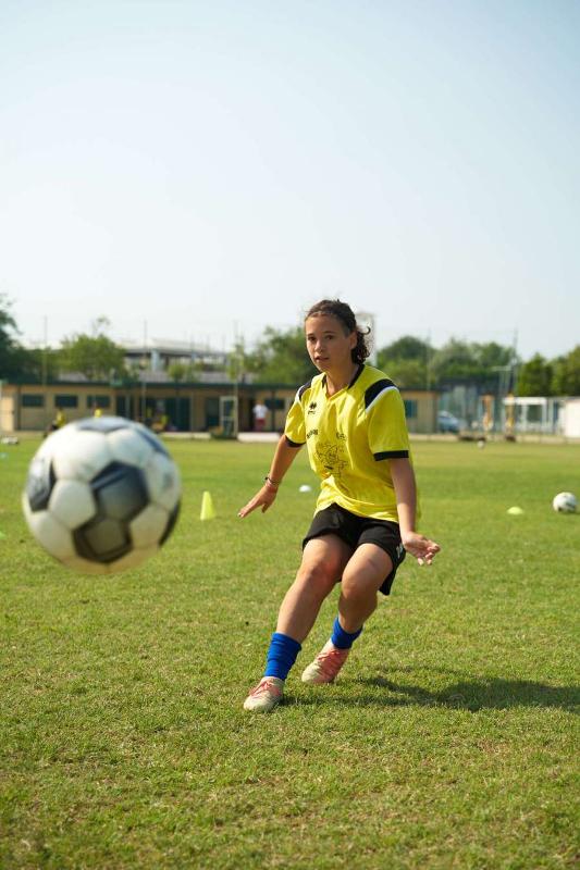 Una ragazza calcia il pallone con precisione al campo estivo calcio