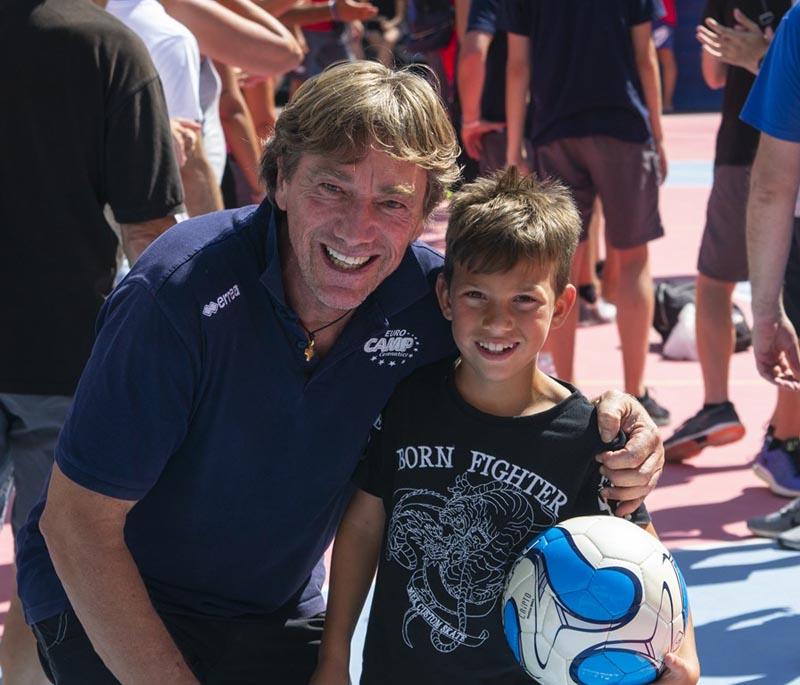 Un allenatore e un bambino con il pallone in mano sorridono insieme al campo estivo calcio