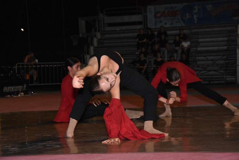 Una ragazza vestita di nero e rosso esegue una mossa di ballo sul palco di sera al campo estivo danza