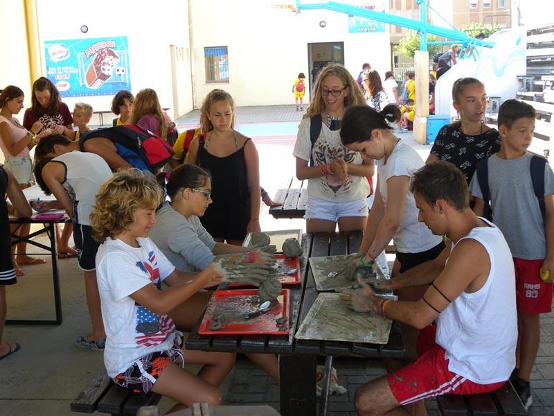 Alcuni ragazzi seduti sui tavoli utilizzano l'argilla per creare delle forme al campo estivo sport & fun