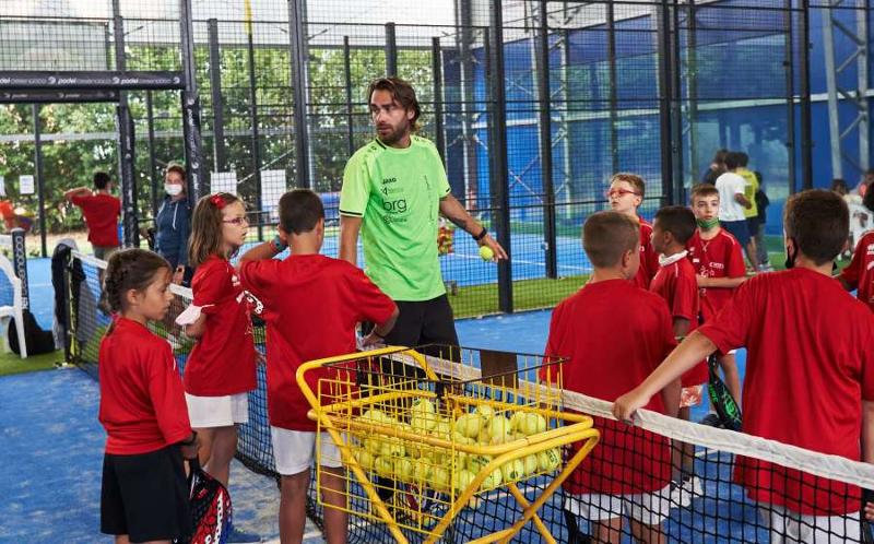 Un allenatore di paddle insegna a dei bambini vestiti di rosso dentro al campo da gioco presso il campo estivo sport & fun