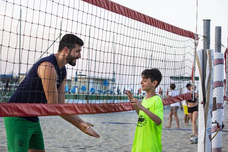 Durante il campo estivo pallavolo al mare un istruttore batte il cinque a un bambino sotto rete