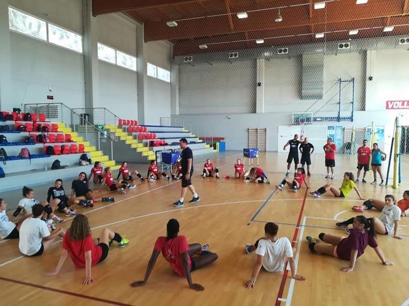 Durante il campo estivo pallavolo i ragazzi siedono in cerchio attorno all'allenatore che spiega in palestra