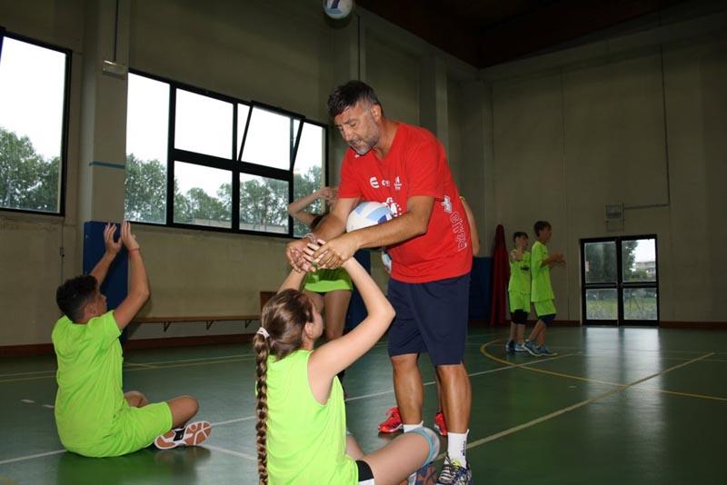 Al campo estivo pallavolo l'istruttore vestito di rosso aiuta la ragazza a tenere le mani correttamente per eseguire un palleggio