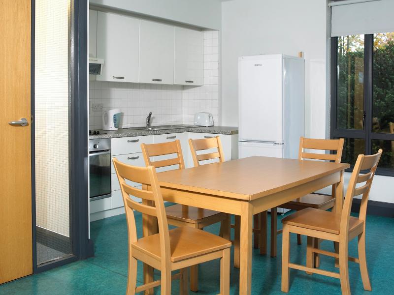 Nella foto vi è un grande tavolo con alcune sedie con una cucina dietro che si trova nella residenza del soggiorno linguistico Dublino
