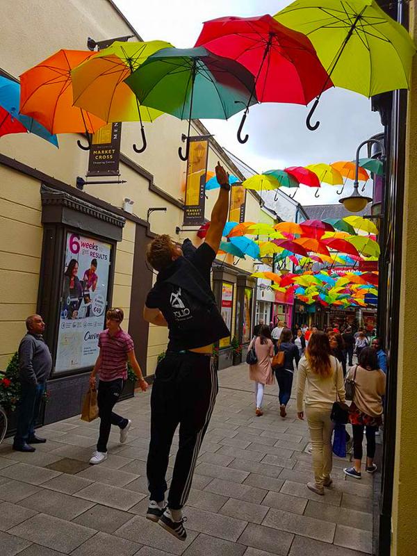 Ragazzi che camminano per le vie della città e un ragazzo prova a toccare saltando gli ombrelli colorati che fungono da decorazione durante il soggiorno linguistico Dublino