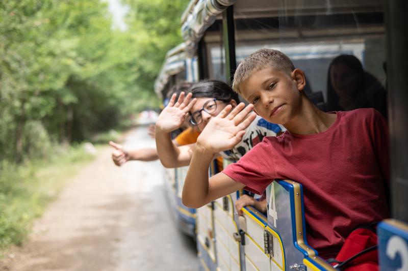 Tre bambini sul trenino turistico salutano con la mano al campo estivo Abruzzo