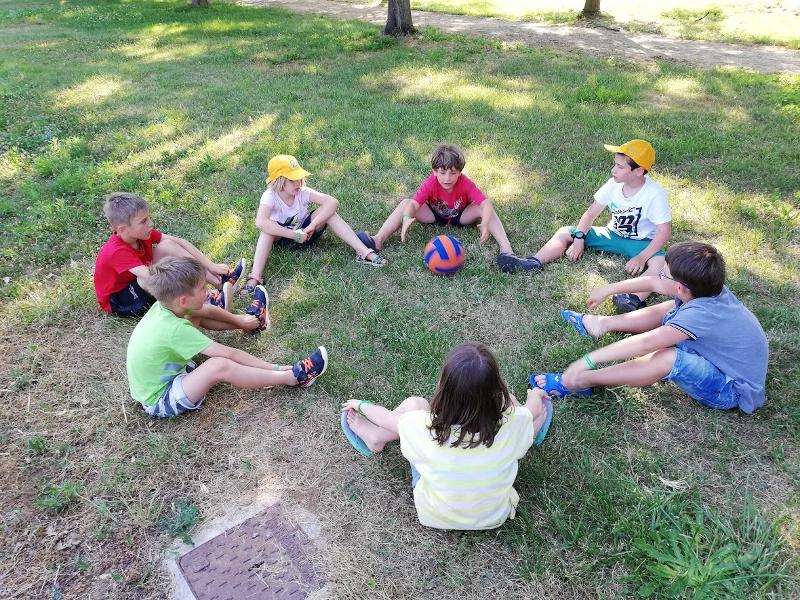 Al campo estivo bambini alcuni bambini siedono sul prato giocando a palla