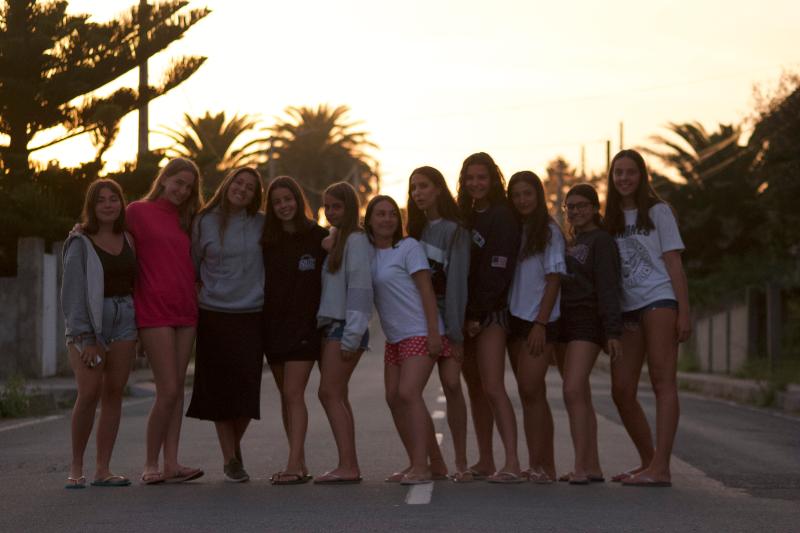 un gruppo di ragazze del campo estivo surf si riunisce in mezzo alla strada per una foto al tramonto
