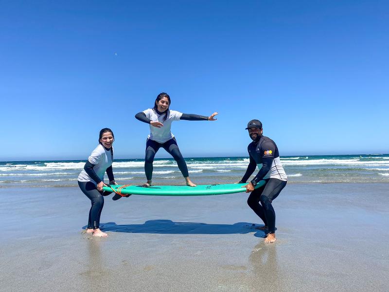 Due amici del campo estivo surf sollevano e reggono in equilibrio una ragazza sulla tavola
