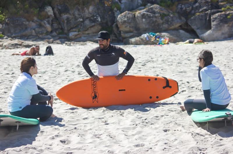 Due giovani partecipanti ascoltano con attenzione l'istruttore del campo estivo surf
