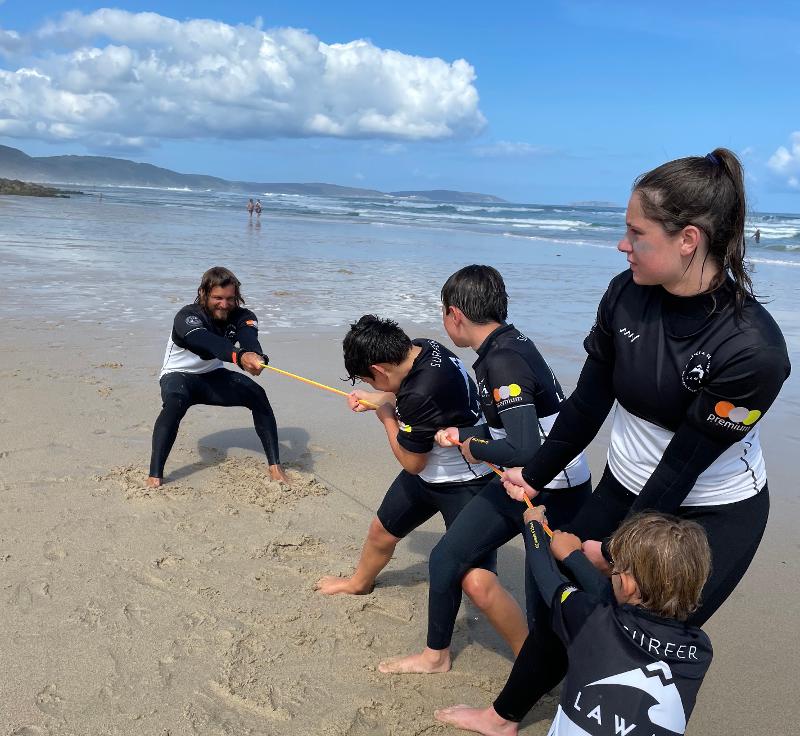 I partecipanti del campo estivo surf giocano al tiro con la corda in spiaggia