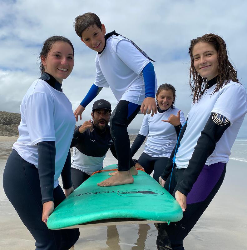 Un bambino è in piedi sulla tavola retta in mano da altri partecipanti e istruttori del campo estivo surf