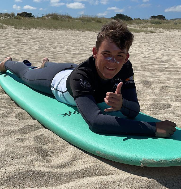 Un ragazzo del campo estivo surf è sdraiato sulla tavola da surf sulla spiaggia