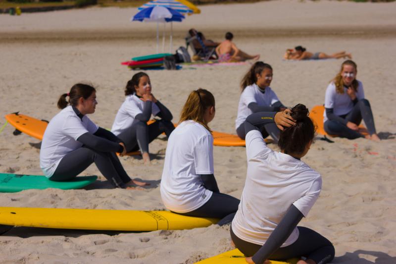 Sei ragazze del campo estivo surf sono sedute sulle loro tavole sulla sabbia e parlano 