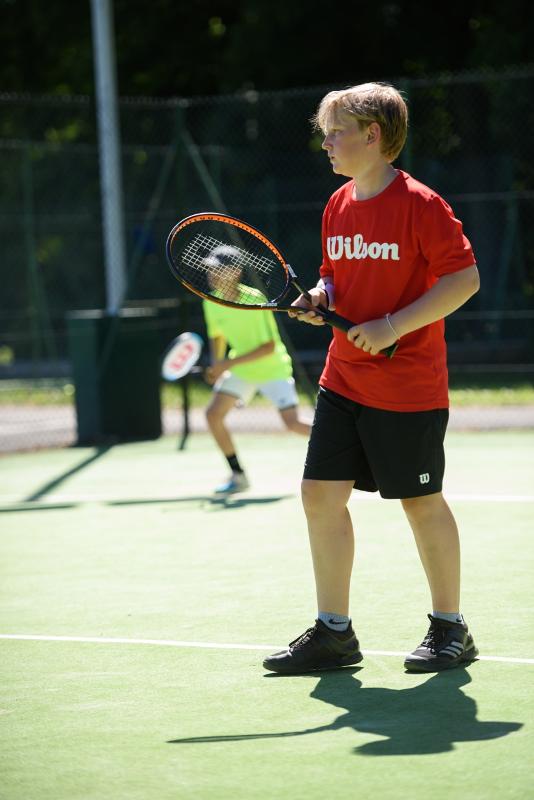 Ragazzo che gioca a tennis indossando una maglietta rossa e impugnando una racchetta al soggiorno in lingua inglese nel cuore della Scozia