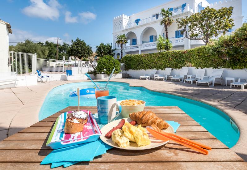 Al soggiorno linguistico francese c'è una piscina con un tavolino dove c'è una colazione ricca sopra