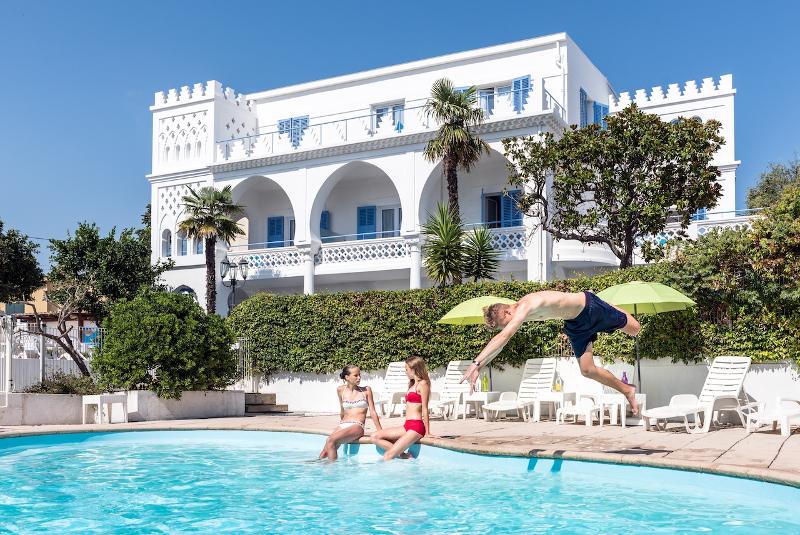 Al soggiorno linguistico francese un ragazzo si sta tuffando in piscina e due ragazze stanno prendendo il sole a bordo piscina