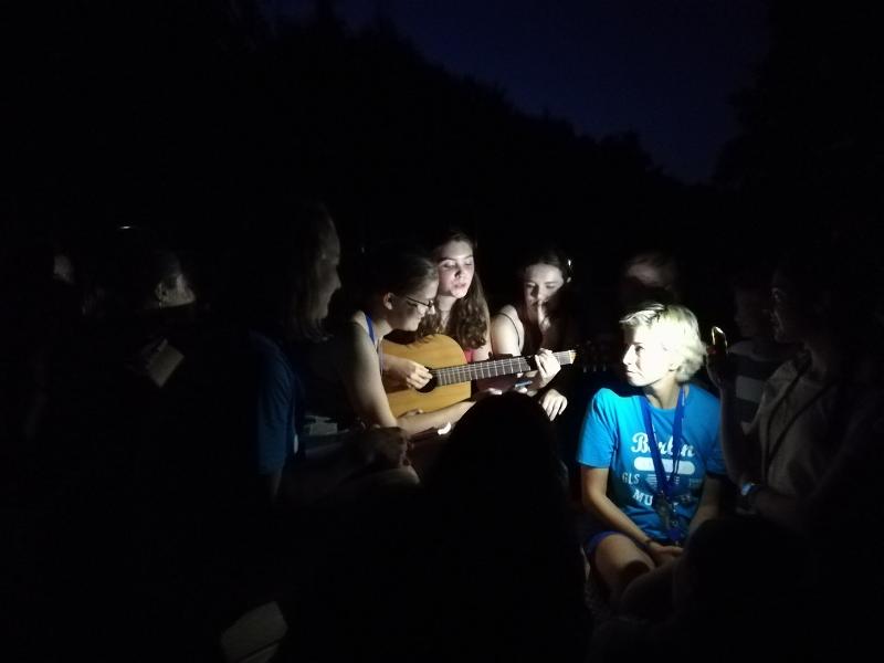 I partecipanti del soggiorno linguistico tedesco ascoltano una ragazza suonare la chitarra durante un'attività serale