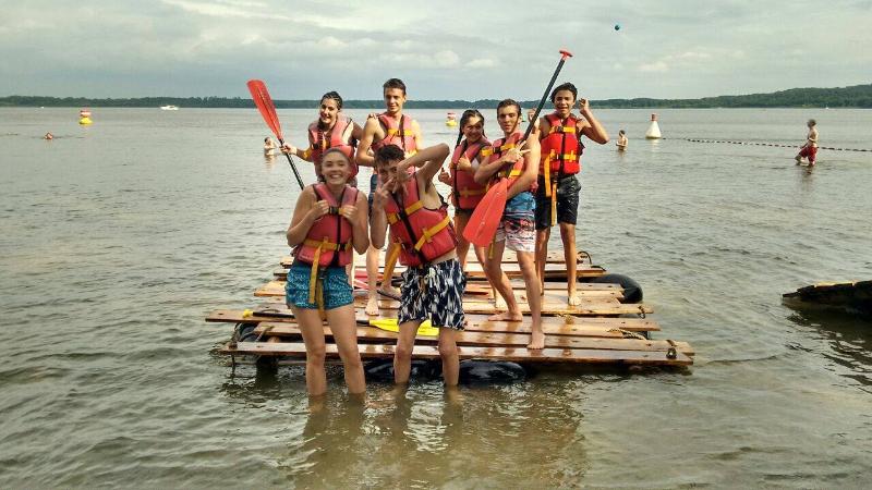 Un gruppo di partecipanti del soggiorno linguistico tedesco è su una piattaforma di legno sul lago e indossa l'abbigliamento necessario per una gita in kayak