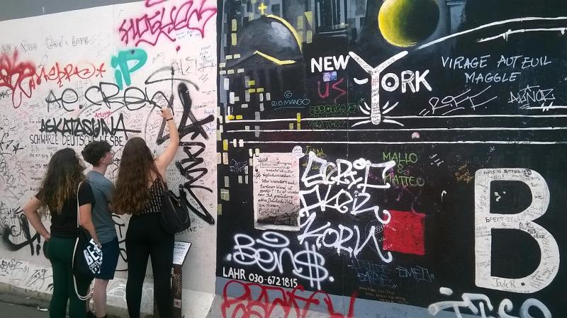 Due ragazze e un ragazzo scrivono la loro firma sul muro di Berlino all'East Side Gallery