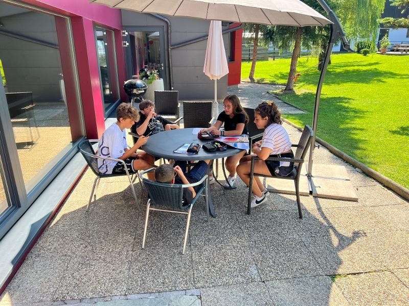 Gruppo di ragazzi fa i compiti all'esterno sotto un ombrellone alla vacanza studio in inglese