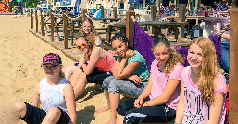 Al soggiorno linguistico inglese estivo a Bournemouth ci sono delle ragazze che sono sedute in spiaggia che sorridono 