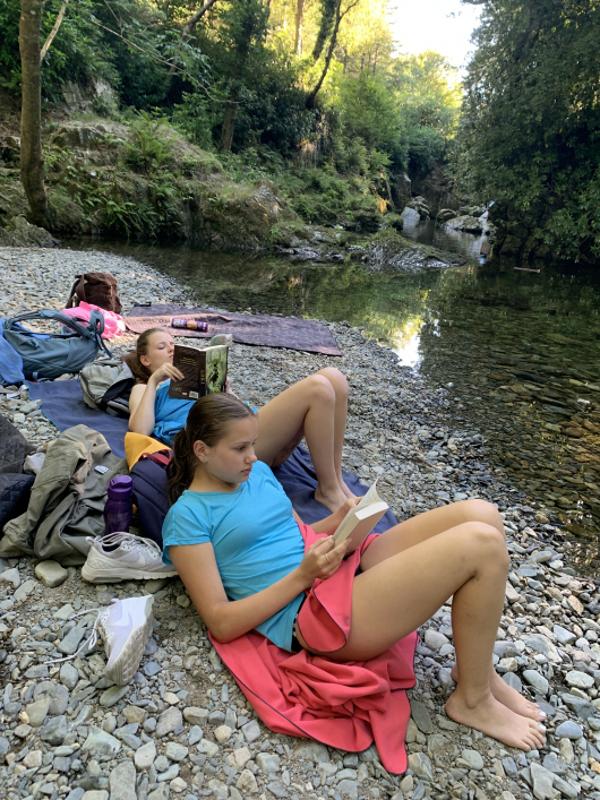 Due ragazze del campo internazionale outdoor leggono in riva al fiume