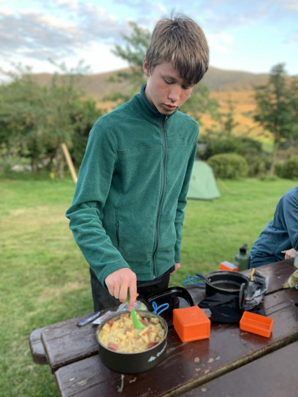 Un ragazzo del campo internazionale outdoor cucina una pasta col fornello da campeggio
