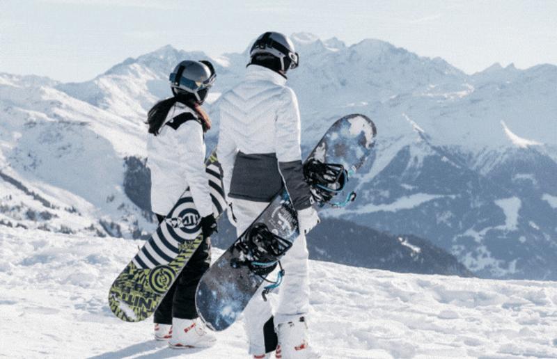 dei ragazzi vestiti da sci sollevano le loro tavole da snowboard divertendosi alla fine della pista