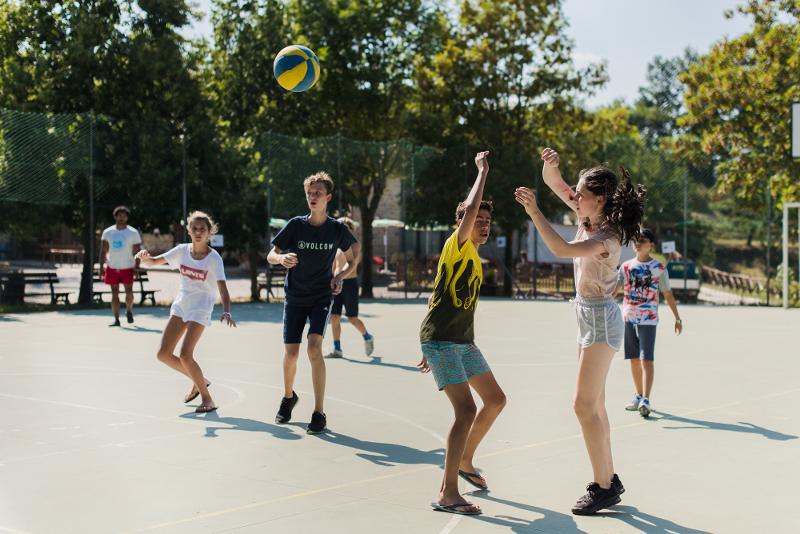 Al campo estivo inglese a Valbonella ci sono dei ragazzi che stanno giocando a basket nel campetto