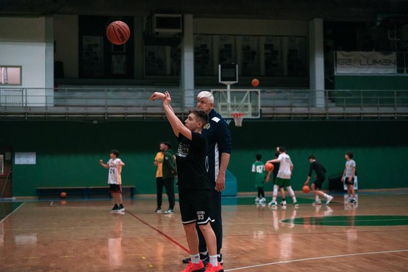 Al campo estivo di basket un ragazzo sta facendo un tiro a canestro insieme all'allenatore