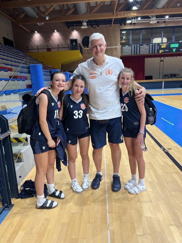 Al campo estivo di basket tre ragazze stano abbracciando l'allenatore 