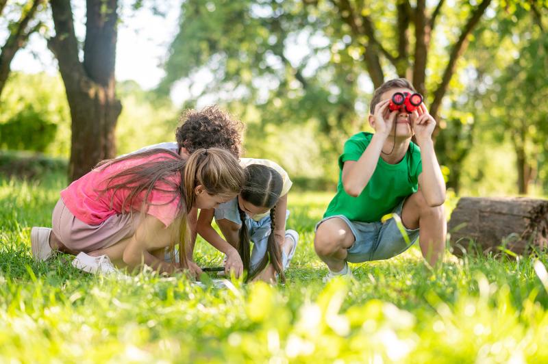Al campo estivo avventura Merano ci sono dei bambini che giocano all'aperto e uno guarda attraverso un binocolo