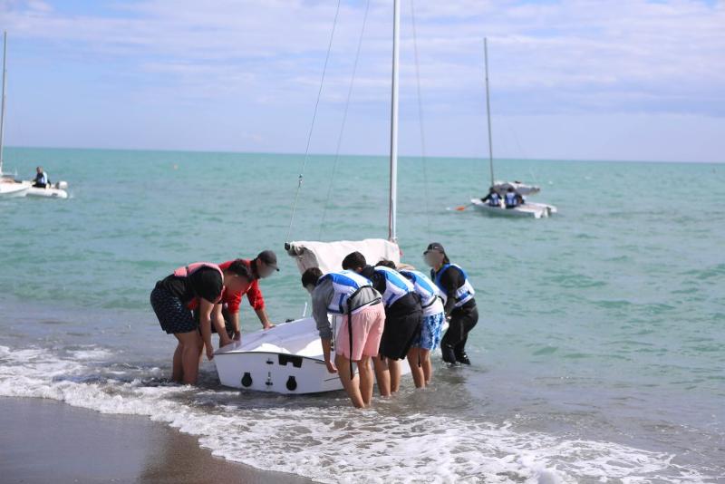 dei ragazzi a riva spingono una barca a vela in mare